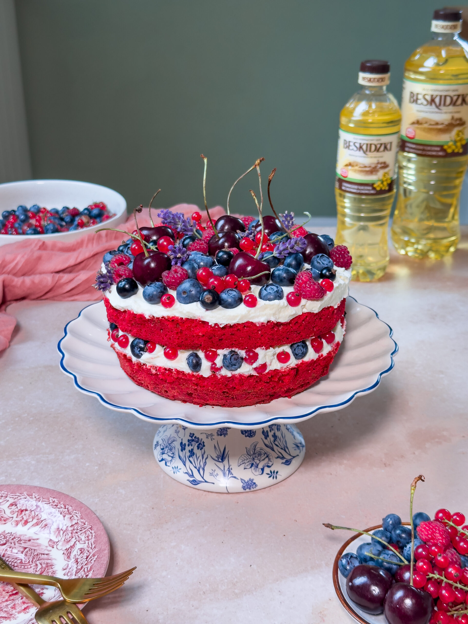 Ciasto red velvet z owocami i kremem śmietankowym, ozdobione malinami, borówkami i czereśniami.